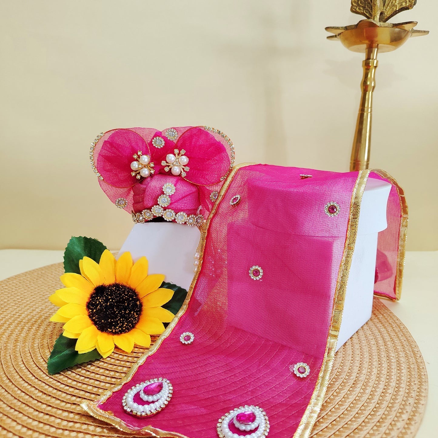 Pink Pagdi with gold border, earrings, and a sunflower decoration on a beige background