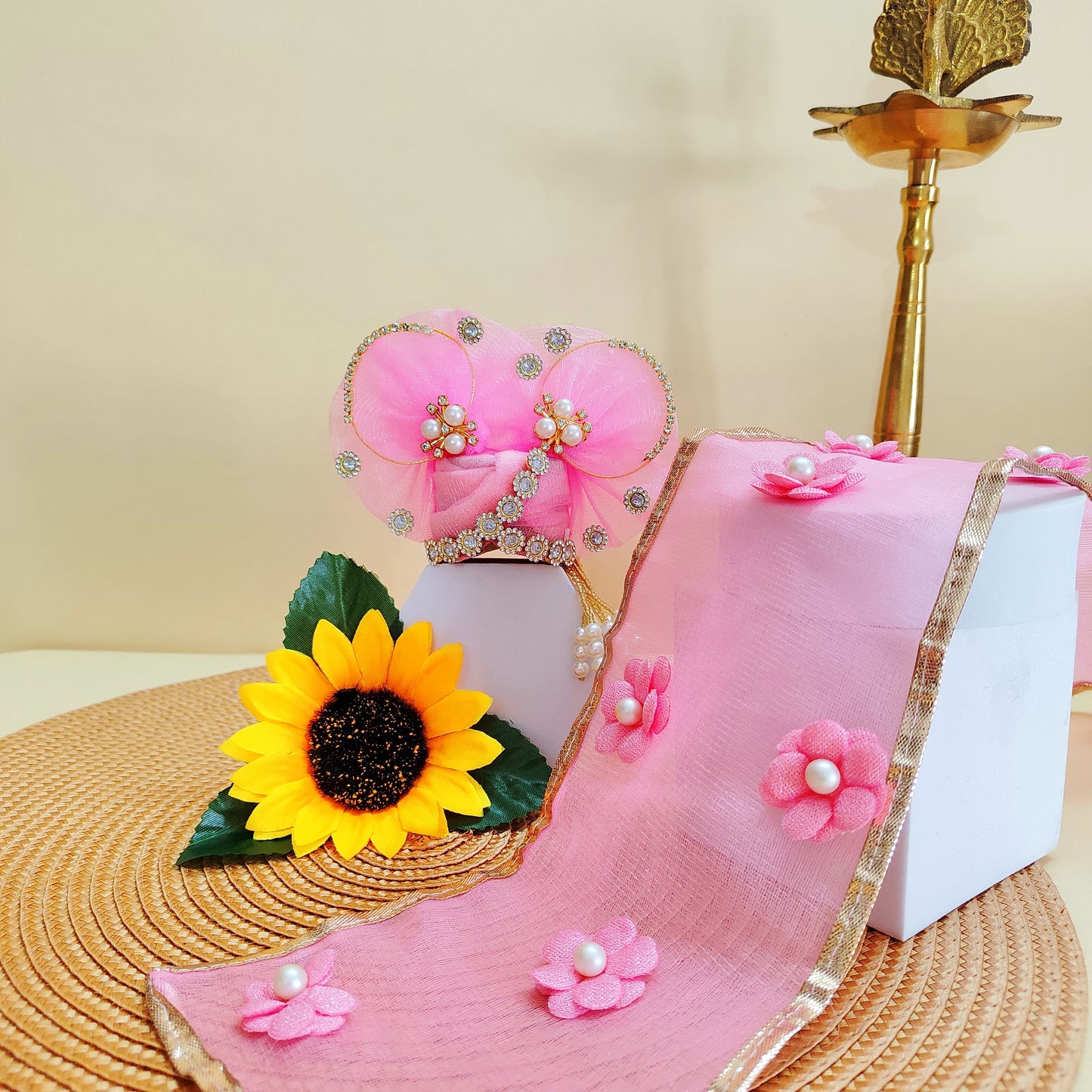 Decorative pink Kanha ji Mukut with flowers and a sunflower on a beige background