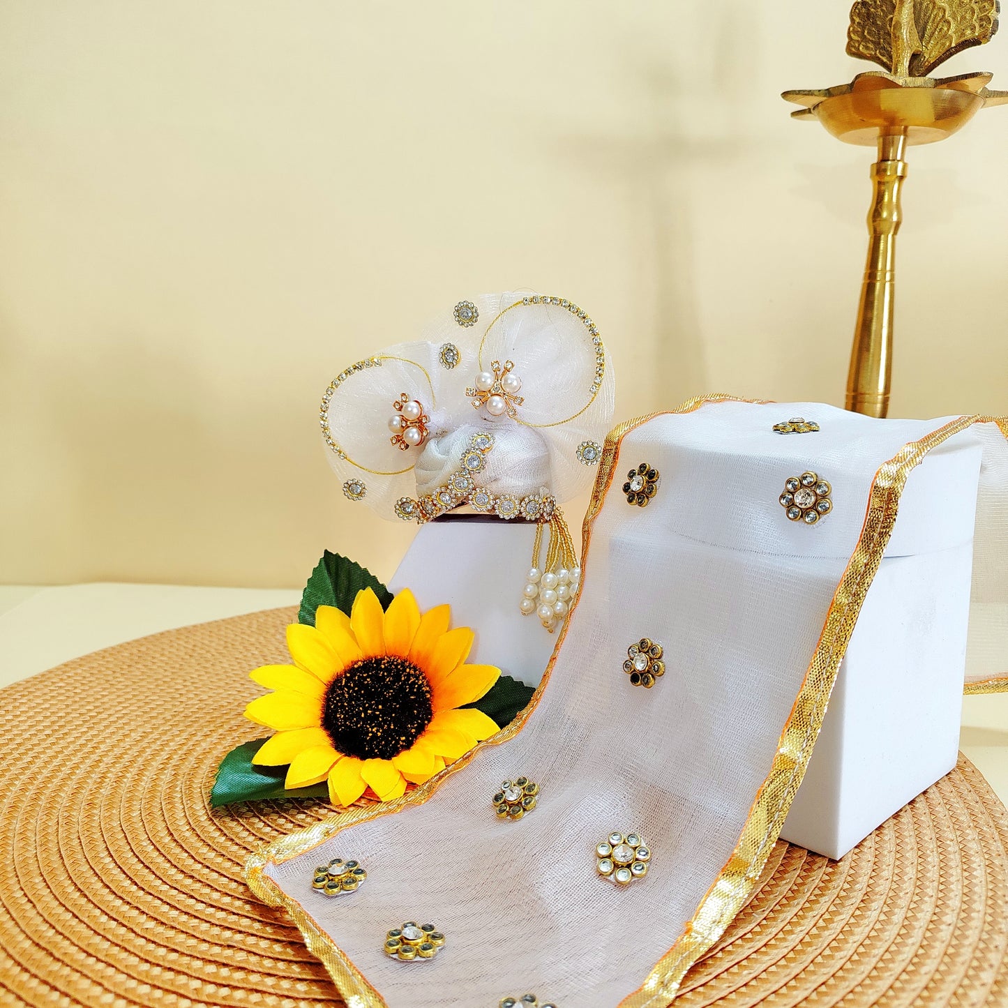 White mukut laddu gopal with gold accents and sunflower decoration on a beige background