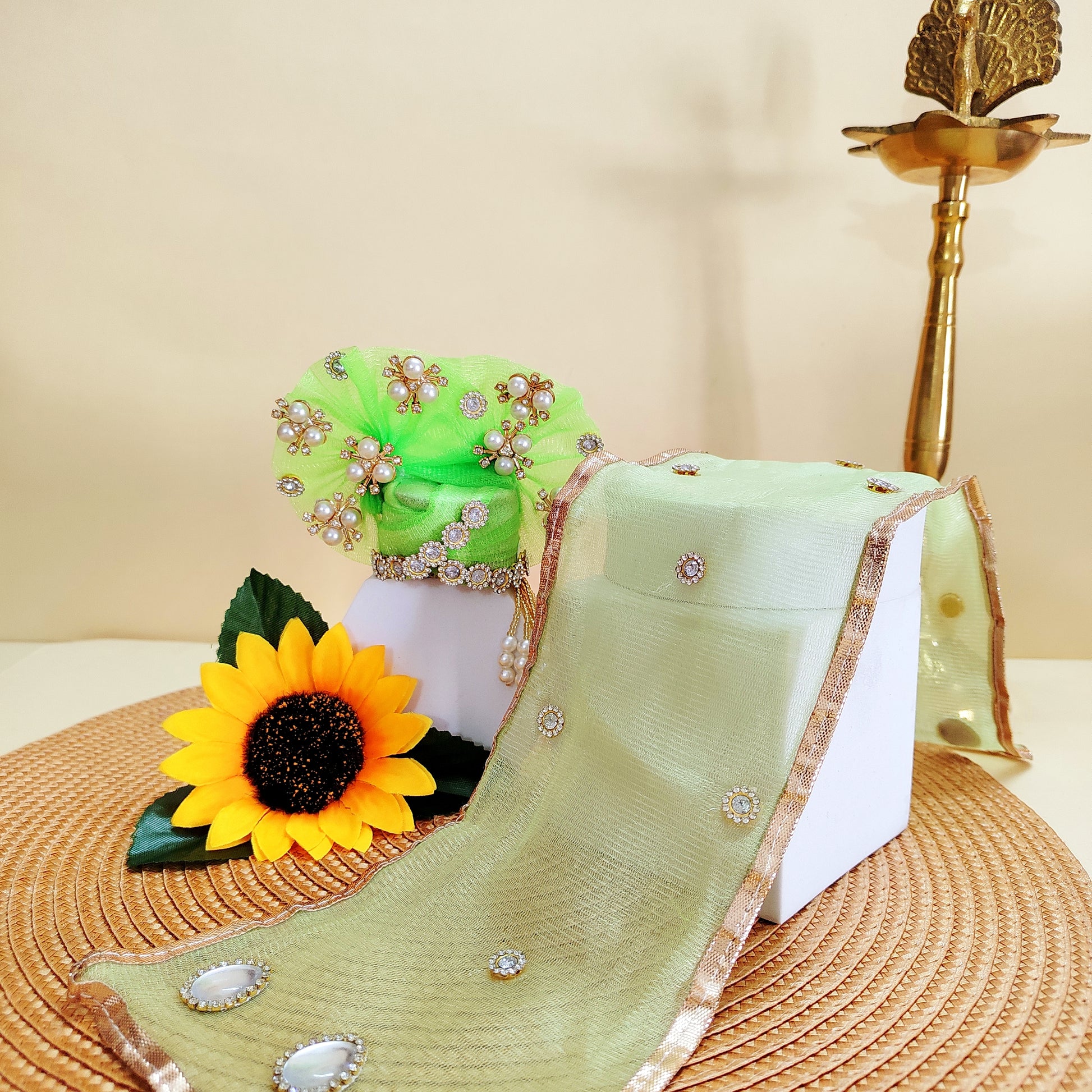 Green mukut with embellishments and a sunflower on a textured surface