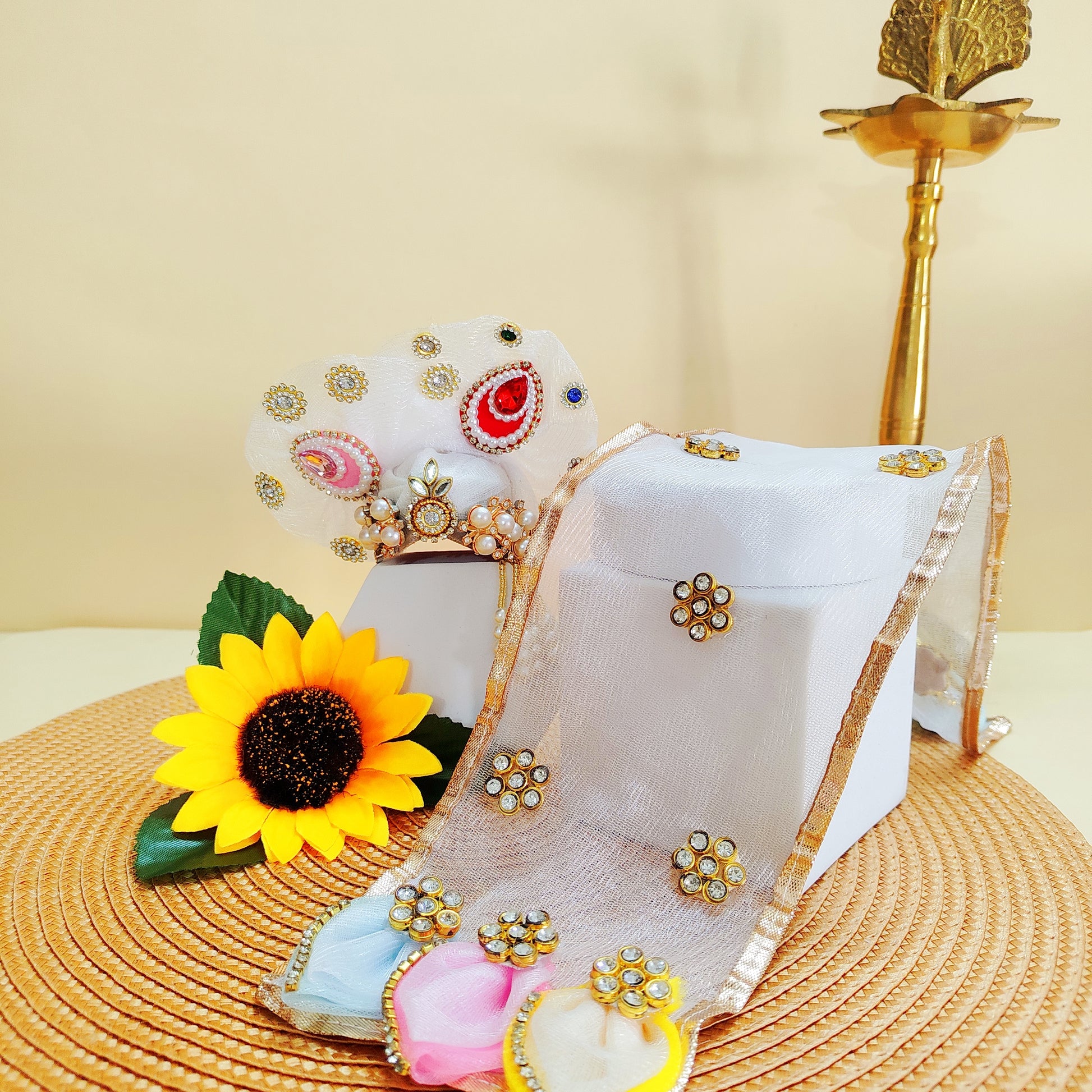 Decorative items including a Mukut and Radha Rani Dupatta sunflower, jewelry box, and decorative elements on a textured surface.